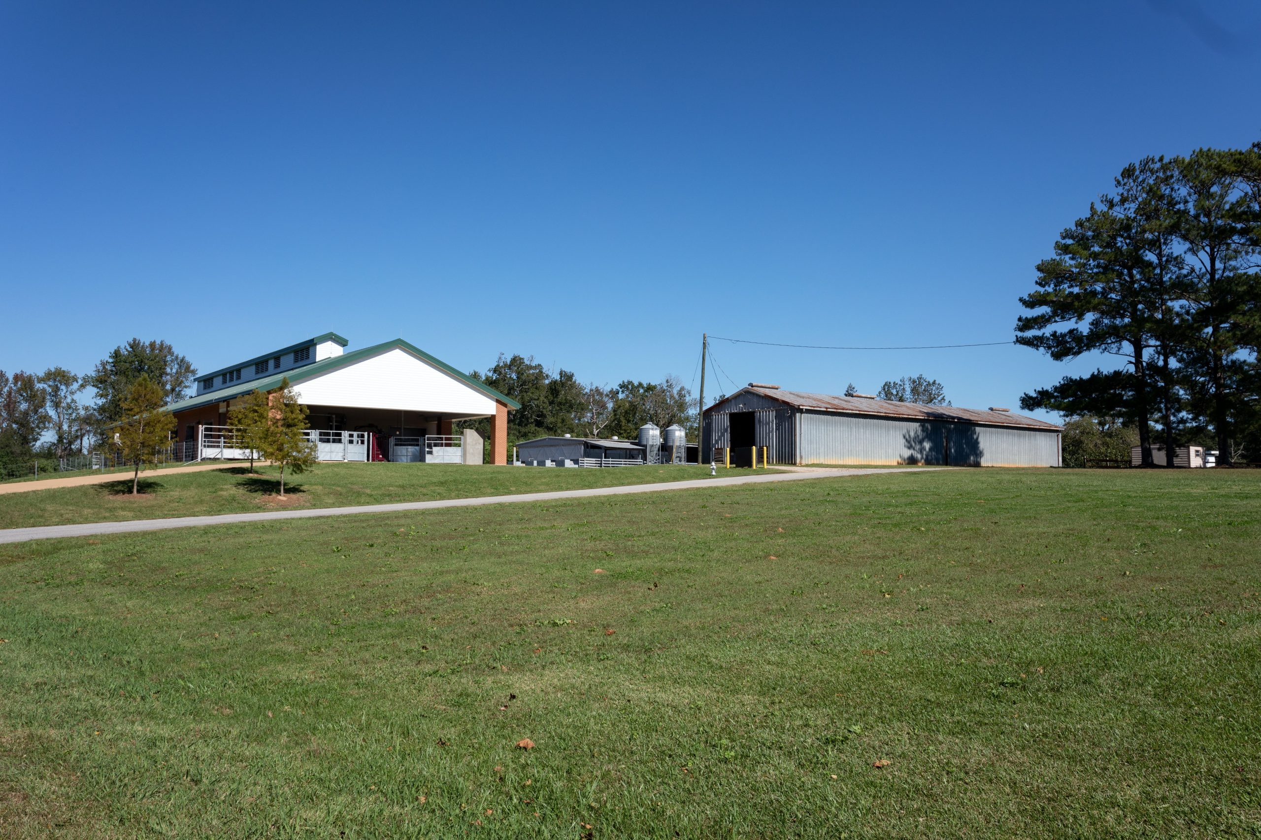 Driveway leading to red brick barn and two silver metal rectangular buildings